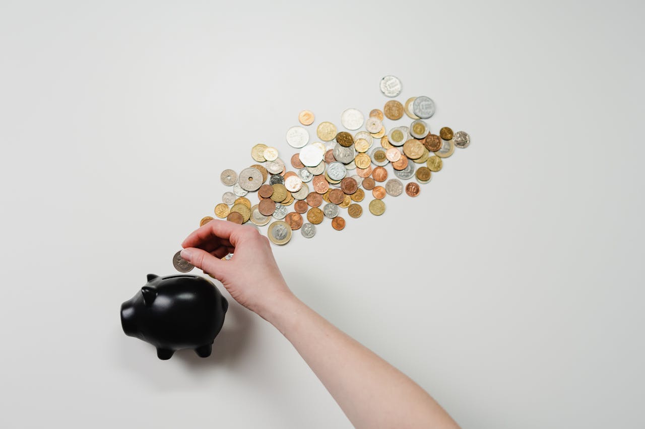 creative Person placing coin into a black piggy bank with scattered coins, symbolizing savings and finance.